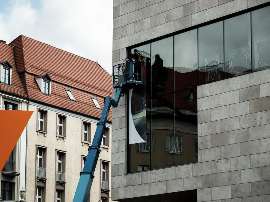gallery-03 A man cleaning skyscraper windows with a harness, showcasing urban high-rise work.